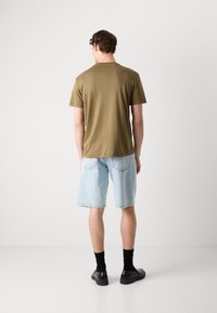 Oliven grønn t-skjorte med korte ermer og rund hals, kombinert med lyseblå denimshorts og svarte sko, sett fra baksiden.