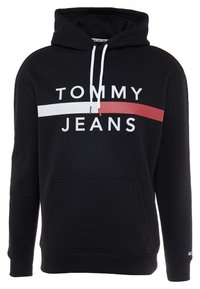 Černá mikina s kapucí a přední kapsou, bílé šňůrky, velký nápis "TOMMY JEANS" a bílý a červený vodorovný pruh přes hruď.