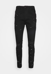 Mustat farkut slim fit -mallilla, joissa on kuluneet paikat ja hajallaan valkoisia yksityiskohtia. Klassinen napitus ja taskut.