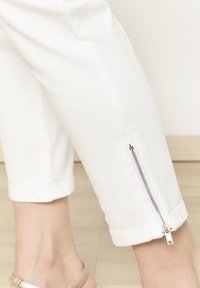 Witte, aangesloten cropped broeken met een ritsdetail bij de manchetten, met een gladde textuur en rechte snit. Lichte vloer in de achtergrond.