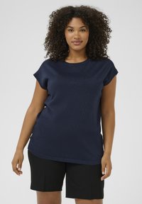 Mørkeblå kortærmet top med en glat, let reflekterende tekstur. Crew neck-design, parret med ensfarvede sorte shorts.