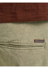 Gros plan sur la poche d'un pantalon beige texturé avec une petite étiquette en cuir marron et un tissu marron au-dessus.