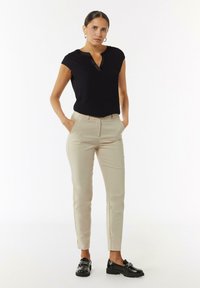 Zwart T-shirt met korte mouwen van een lichtgewicht stof en een knoopsluiting, gecombineerd met beige slim-fit broek en zwarte loafers.