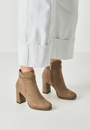 Hellbraune Wildleder-Stiefeletten mit Blockabsätzen und seitlichen Reißverschlüssen, getragen zu weißen, weit geschnittenen Hosen mit umgeschlagenen Säumen.