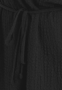 Tissu noir texturé avec une ceinture nouée à la taille. La surface présente un motif froissé, offrant profondeur et dimension.