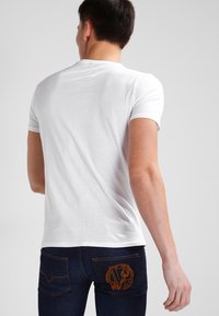 Vit kortärmad t-shirt, i bomullsmaterial, figurnära design, rund halsringning. Mörka jeans med orange broderad logotyp på bakfickan.