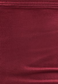 Acercamiento de una tela roja profunda y suave con costuras visibles a lo largo del borde superior.