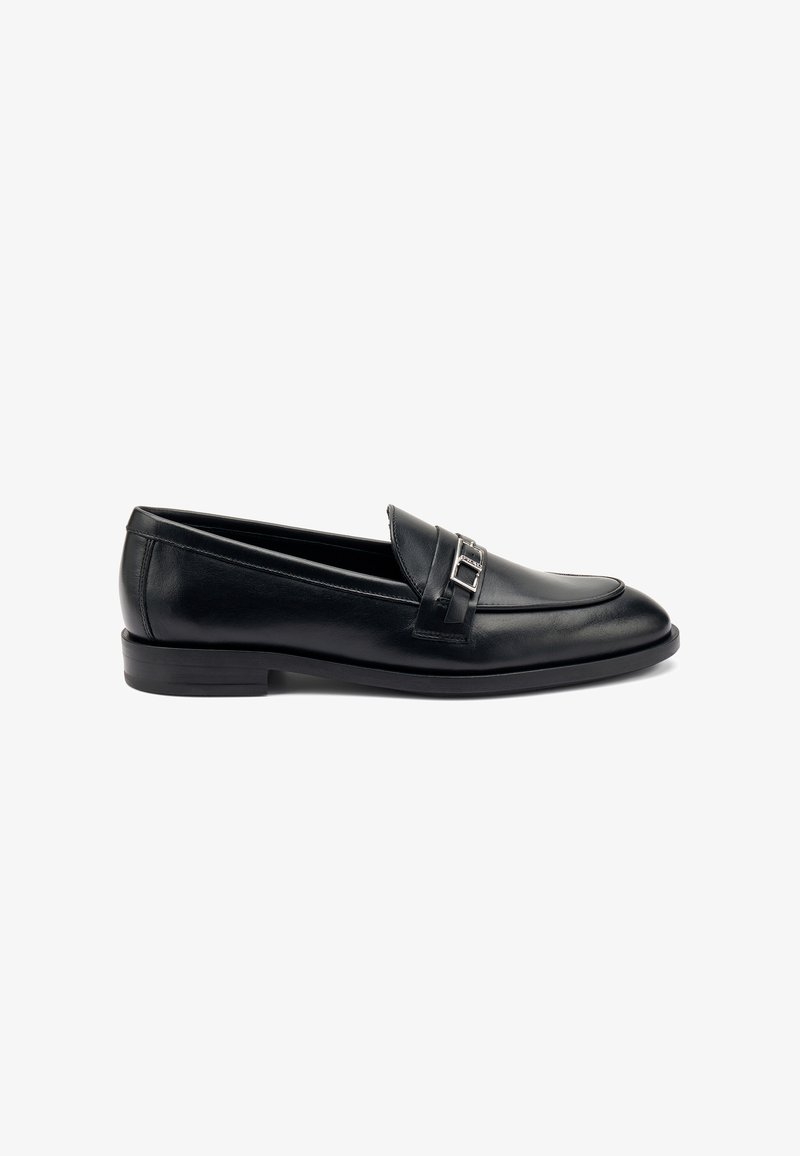 Mocasines de cuero negro con punta redonda, que presentan un acento metálico decorativo en la parte frontal y un tacón bajo en bloque. Textura suave.