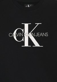 Svart sweatshirt i bomull med texten "CALVIN KLEIN JEANS" i vit fet stil och en framträdande "CK" logotyp. Slät yta.