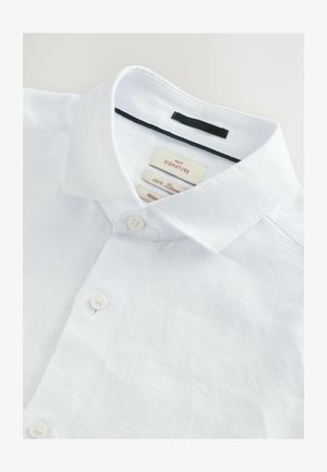 Camisa de lino blanco abotonada con un cuello estructurado, dos botones y un acabado texturizado. Las etiquetas indican "100% lino" y "corte regular".