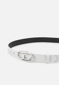 Weißer Leder-Gürtel mit glatter Oberfläche, ausgestattet mit einer silbernen ovalen Schnalle und einem kontrastierenden schwarzen Innenleben. Verstellbar mit mehreren Löchern.