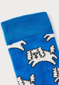 Chaussette en tricot bleu ornée de motifs de chiens blancs ludiques, avec des contours noirs détaillés et une texture douce. Le haut est côtelé pour plus d'élasticité.