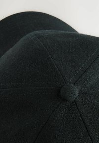 Căciulă neagră dintr-un material texturat, având vârful rotund, detalii de cusătură și un accent central cu un buton pe coronă.