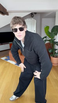 Fekete polárdzseki cipzárral és elülső zsebbel, fekete bőszárú nadrág, ezüst tornacipő. A sötét napszemüveg teszi teljessé a szettet.