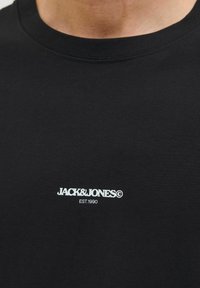 Sort bomuld t-shirt med rund hals og korte ærmer har et hvidt logo, der står "JACK&JONES EST.1990" på forsiden.