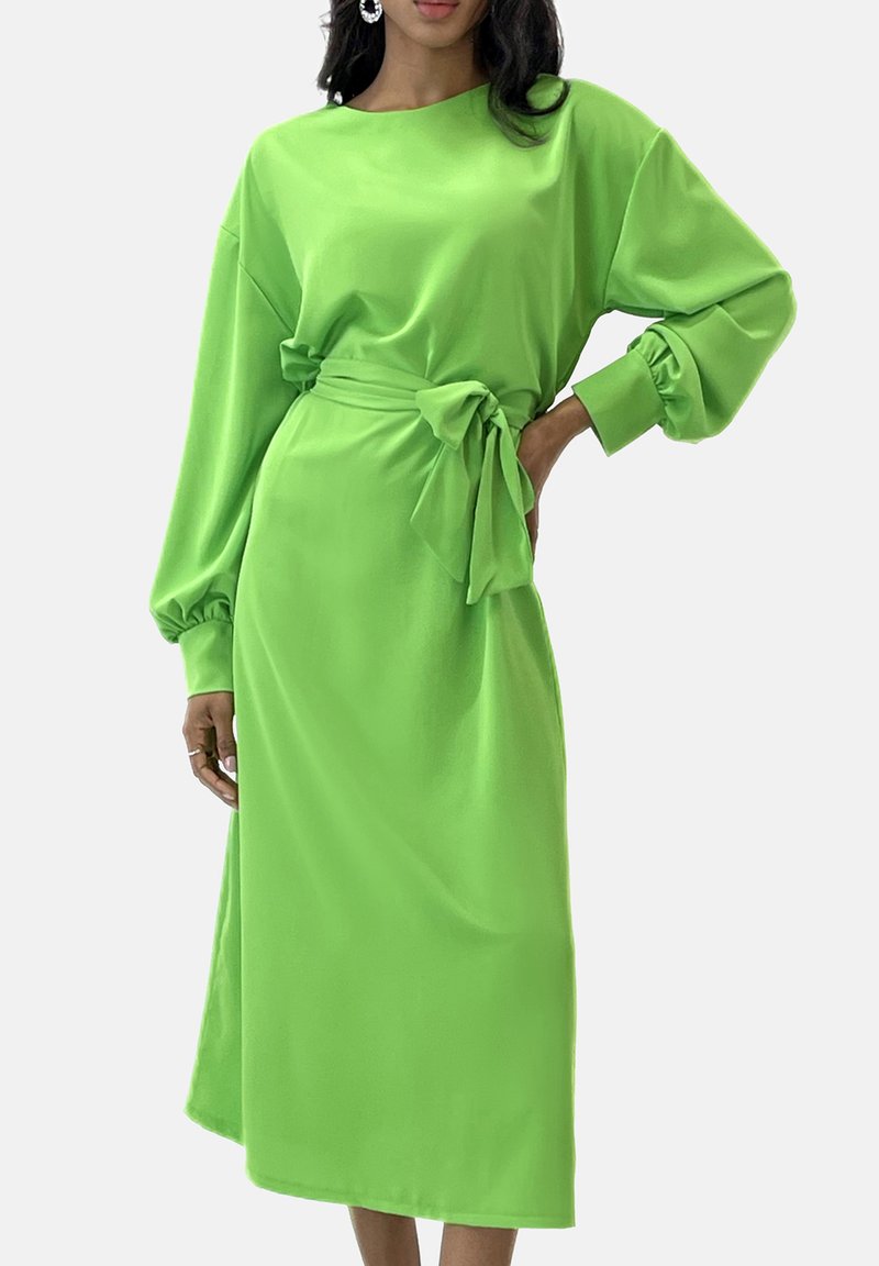 Groene jurk met lange mouwen van gladde stof en een taille die wordt benadrukt met een ceintuur. Heeft opgeblazen mouwen en een midi-lengte. Eenvoudig, effen ontwerp zonder patronen.