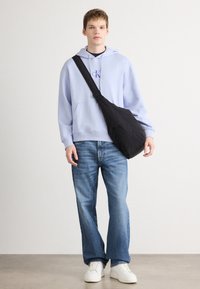 Svetlomodrá mikina s kapucňou a predným vreckom, doplnená modrými džínsami a bielymi teniskami. Čierna crossbody taška s hladkým povrchom.