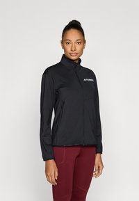 Fekete, könnyű dzseki magas gallérral, teljes cipzárral és mellzsebbel. Bal felső oldalon logóval és testre szabott szabással.