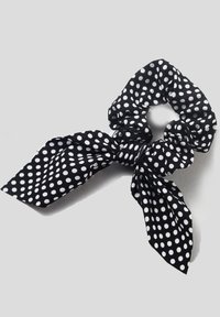 Melna un balta punktiņa scrunchie ar lentu akcentiem, izgatavota no mīksta auduma, ar elastīgu joslu un teksturētu virsmu.