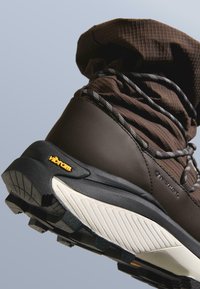 Bocanc maro pentru drumeții cu partea superioară texturată, talpă Vibram, accente negre și un model robust al tălpii pentru aderență.