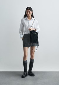 Camisa blanca de botones, falda mini de ante gris, bolso cruzado negro con flecos, botas negras hasta la rodilla, calcetines con detalles en gris. Estilo simple y moderno.