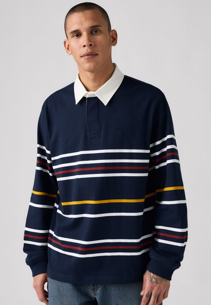 Polo de manga larga azul marino con cuello blanco, con rayas horizontales en blanco, rojo y amarillo. Hecho de una mezcla de algodón.