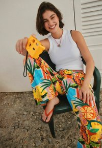 Farebné tropické nohavice s širokými nohavicami v jasných žltých, zelených a ružových farbách; kombinované s bielym tielkom a oranžovými žabkami.