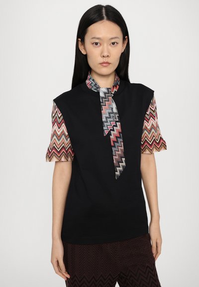 Μαύρη μπλούζα με κοντά μανίκια σε πολύχρωμο ζιγκ-ζαγκ σχέδιο και patterned γραβάτα. Φτιαγμένη από μαλακό ύφασμα, διαθέτει ψηλό κολλάρο.