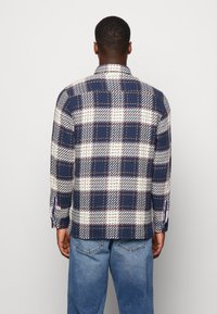 Camicia con bottoni realizzata in tessuto intrecciato con un motivo a scacchi blu e bianchi, dotata di maniche lunghe e spacchi laterali all'orlo.