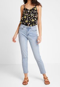 Top a righe nere con fiori e spalline sottili, abbinato a jeans a vita alta di colore blu chiaro. Sandali marroni con cinturini completano l'outfit.