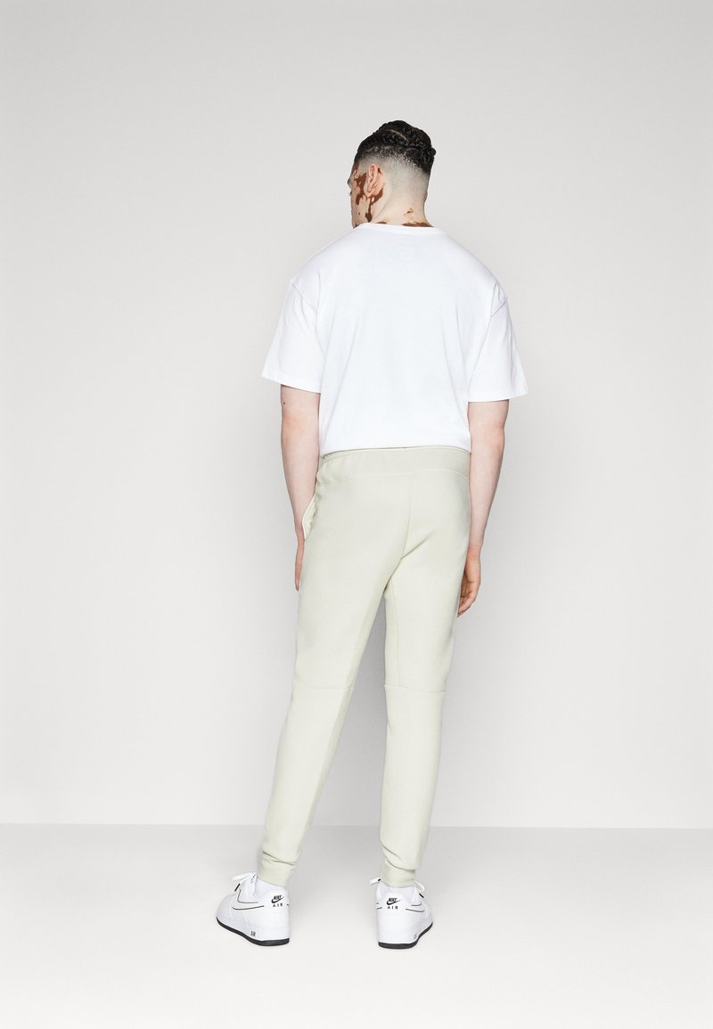 Helle Sweatpants mit einem schmal zulaufenden Schnitt, kombiniert mit einem schlichten weißen T-Shirt. Weiße Sneaker mit schwarzen Akzenten runden das Outfit ab.
