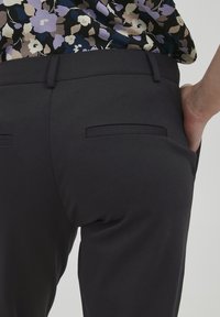 Svarta skräddarsydda byxor i en mjuk tyg, med två bakfickor och en smal passform, kombinerade med en färgglad blommönstrad topp.