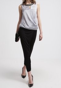 Haut sans manches argenté avec un design drapé et un col orné de perles, associé à un pantalon noir ajusté et des talons noirs.