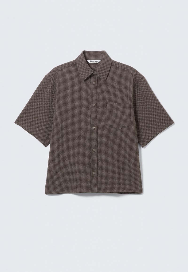 Chemise marron à manches courtes avec boutons, motif gaufré texturé et poche poitrine, posée à plat sur un fond clair.