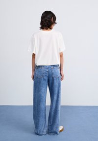 White cotton t-shirt paired with light blue wide-leg denim jeans, featuring rear pockets and a relaxed fit. Plain design, minimal detailing.