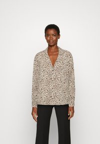 Blusa com padrão de leopardo em bege e castanho, com decote em V profundo e mangas longas. Tecido suave e corte descontraído, combinada com calças pretas.
