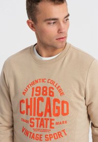 Felpa beige con grafica rossa "Chicago 1986 Authentic College", girocollo e polsini a coste. Morbido misto cotone.