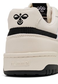 Sneaker bianca con pelle testurizzata, accento nero e logo distintivo sul tallone. Presenta una suola in gomma e cuciture lisce.