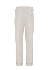 Pantalon beige clair sur mesure en tissu texturé, avec une taille mi-haute, une poche arrière et des revers de pantalon roulés. Deux plis devant.