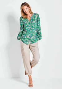 Groene bloemen blouse met knopen en lange mouwen; beige cargobroek met elastische boorden en zijzakken; tan sandalen.