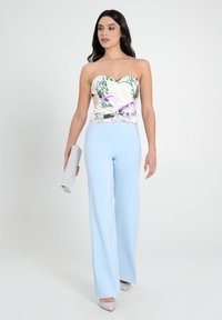 Top floreale senza spalline di colore bianco con motivi verdi e viola, abbinato a pantaloni a gamba larga di un blu chiaro. Il modello tiene una pochette argento.