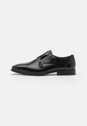 Black leather dress shoe with a pointed toe, featuring dual buckles and a smooth finish. Low heel and sleek, simple design.