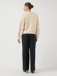 Strickpullover in Creme mit offenen, gemusterten Ärmeln; kombiniert mit schwarzen, weit geschnittenen Jeans und spitzen Absätzen, von hinten gesehen.