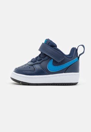 Blue leather sneaker with white sole, featuring a Velcro strap, blue accent logo, and textured upper for durability and support.