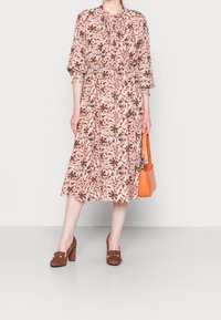 Blommig midiklänning i krämfärg med rosa, bruna och gröna mönster; puffärmar; åtsittande midja. I kombination med bruna klackar och en orange väska.