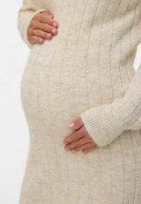 Raseda inimene, kes kannab beeži sooniku muster s-värvi särk, hellalt hoiab oma kõhtu mõlema käega.