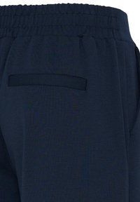 Pantalon bleu marine avec taille élastique et une poche arrière horizontale unique sans fermeture visible.