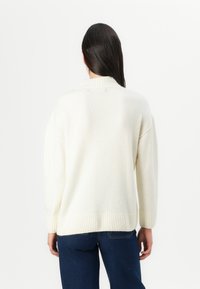 Weißer, übergroßer Pullover mit strukturiertem Finish und geripptem Kragen sowie Bündchen. Kombiniert mit dunkelblauen Jeans, was einen lässigen Stil zeigt.