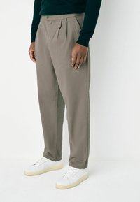 Gray pleated trousers made of lightweight fabric, featuring a tailored fit and side pockets, paired with white sneakers.