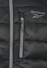 Crna podstavljena jakna siva municija i Reebok logo. Ima dva džepa sa zatvaračem i kviltanu teksturu. Lagani materijal.